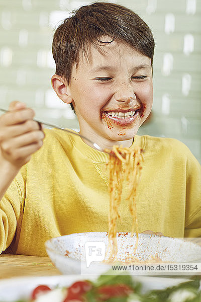 Messy boy eating spaghetti with tomato sauce