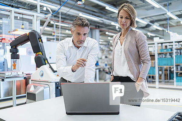 Geschäftsmann und Geschäftsfrau mit Laptop im Gespräch in einer modernen Fabrikhalle