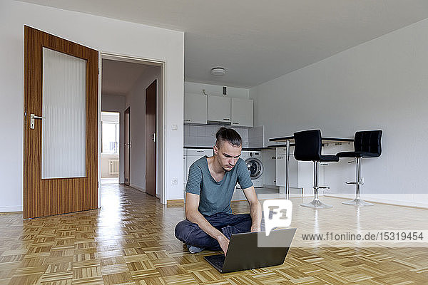 Junger Mann sitzt in einer leeren Wohnung und benutzt seinen Laptop