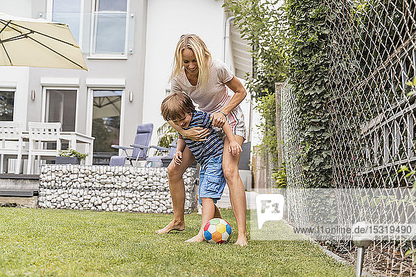 Glückliche Mutter und Sohn spielen im Garten Fussball