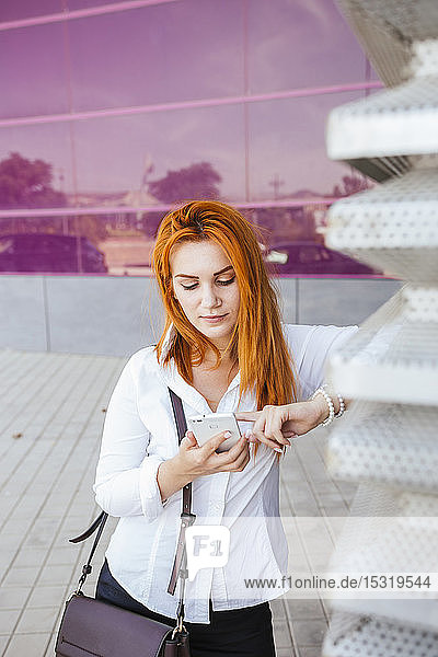 Geschäftsfrau mit Smartphone vor einem modernen Geschäftsgebäude