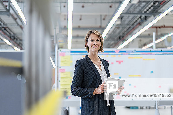 Portrait of confident businesswoman with tablet in a factory hall