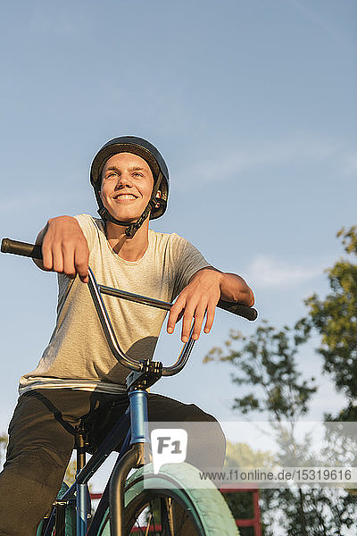 Lächelnder junger Mann mit BMX-Rad im Skatepark bei einer Pause