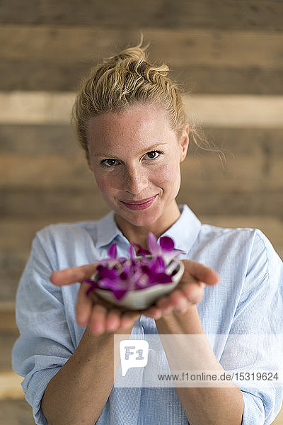 Smiling blond woman holding bowl with orchid petals  blue background