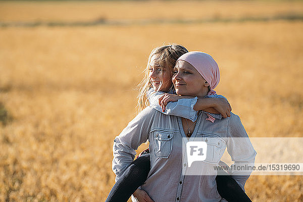 Eine Frau mit Krebs trägt ihre Tochter auf dem Rücken und schaut zur Seite