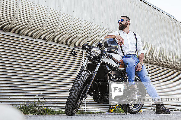 Bearded motorcyclist with sunglasses leaning on his motorbike