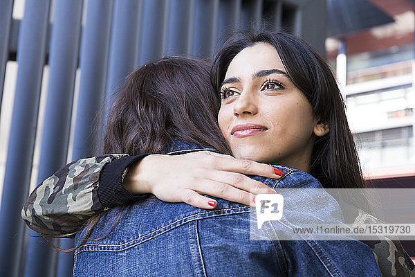 Cheerful young woman looking away and hugging with her friends at a wall