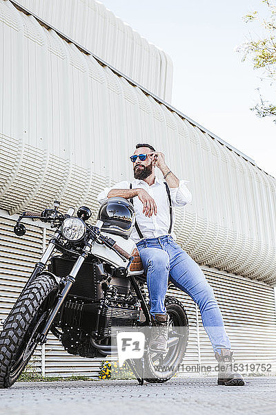 Portrait of bearded motorcyclist with mirrored sunglasses leaning on his motorbike