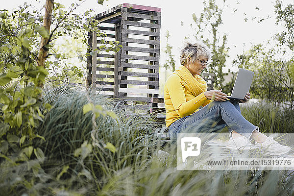 Reife Frau sitzt auf Bank im Freien und benutzt Laptop