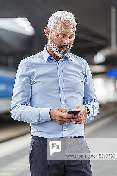 Älterer Geschäftsmann benutzt Mobiltelefon am Bahnsteig