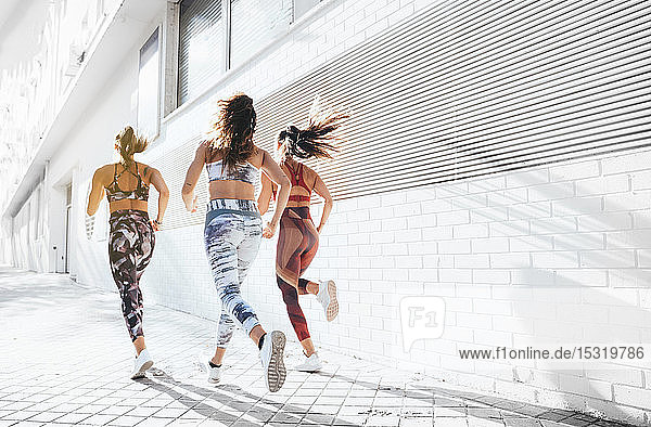 Rückansicht von drei sportlichen jungen Frauen  die in der Stadt laufen