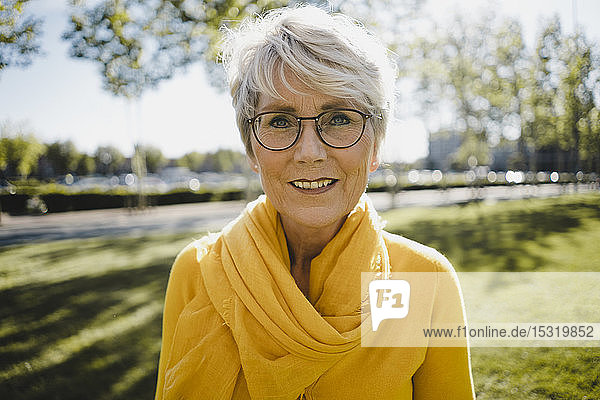 Porträt einer lächelnden reifen Frau mit grauen Haaren  die eine Brille trägt und gelb gekleidet ist