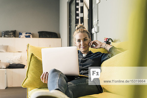 Casual businesswoman using laptop on couch in office lounge