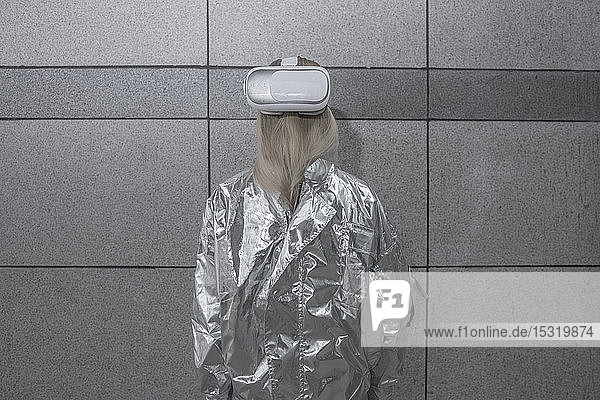 Rear view of girl in silver suit wearing VR goggles on back of head