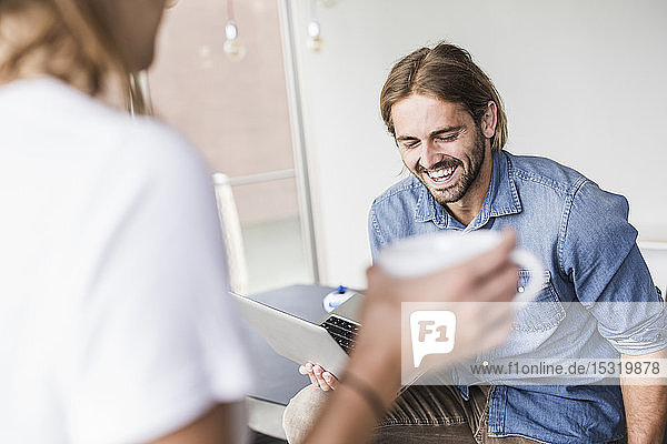 Lachender junger Geschäftsmann mit Laptop und Geschäftsfrau im Büro