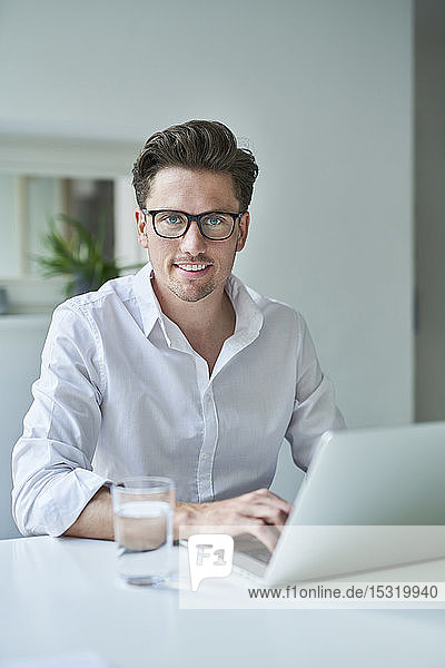 Porträt eines lächelnden Geschäftsmannes mit Laptop im Büro