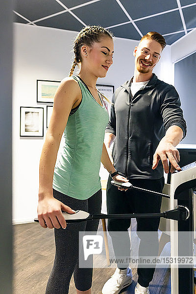 Junge Frau mit Personal Trainerin im Fitness-Studio auf Körperanalysegerät
