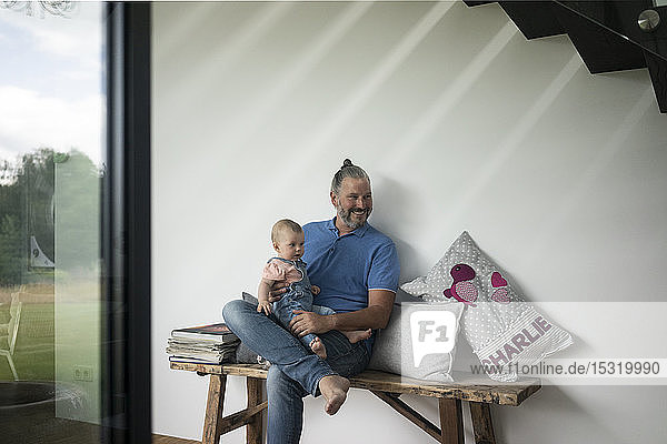Happy mature man sitting with baby girl on a bench at home