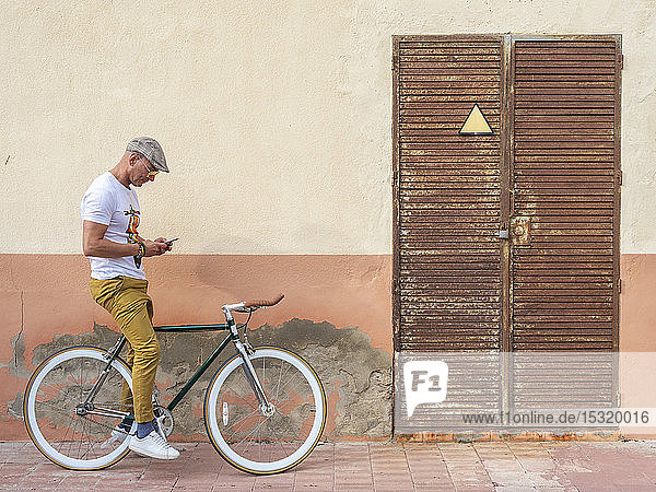 Mann mit Fixie-Fahrrad schaut auf Handy
