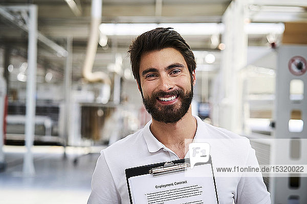 Porträt eines glücklichen Arbeitnehmers mit Arbeitsvertrag in einer Fabrik