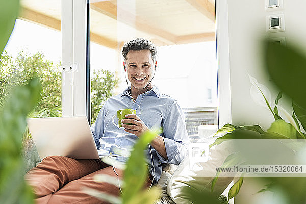 Mature man sitting on couch using laptop drinking coffee