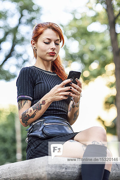 Portrait of red-haired tattooed woman using cell phone outdoors