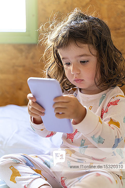Cute little girl in pajamas in bed using mobile phone