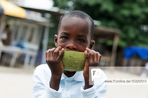 Kind isst mit Liebe eine Wassermelone auf der Straße.