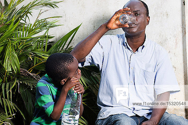 Ein Mann mittleren Alters trinkt Wasser aus einem Glas und ein Kind schaut zu.