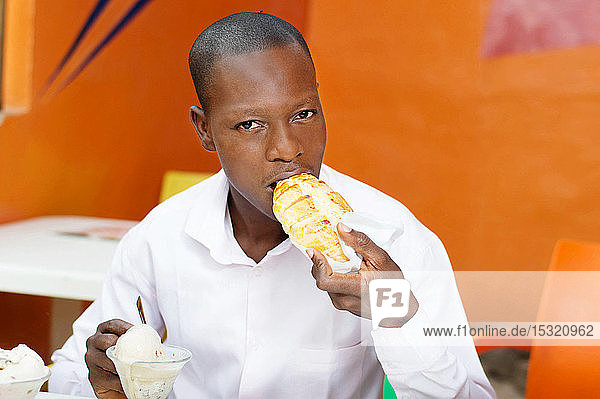 young man sitting in a restaurant eating his bread accompanied by ice.