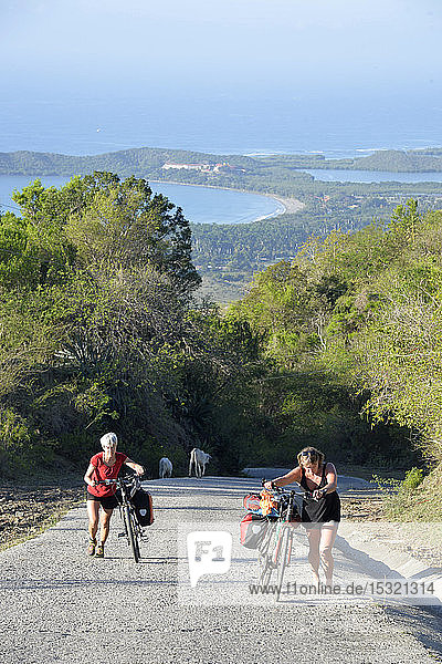 Cuba  eastern region  2 cyclo tourists are pushing their bikes on a way up   we can see the blue ocean down in the back ground