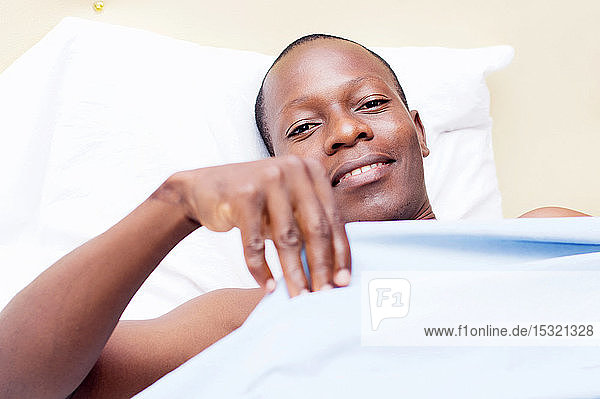 junger Mann auf einem Bett liegend  bereit  in die Kamera zu lächeln.