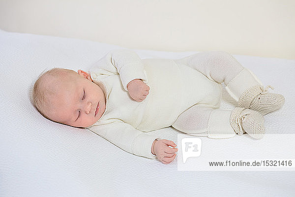 Blick auf einen kleinen Säugling in weißer Kleidung von 2 Monaten  der auf einem weißen Bettchen schläft.
