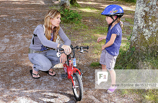 A mother  in her thirties holding the bike of her four-year-old daughter in the forest