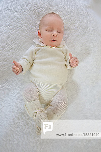 Draufsicht auf einen 2 Monate alten Säugling mit dem Mund im Herzen  der auf einem weißen Bett schläft.