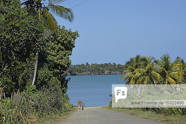 Kuba  Baracoa  Bahia de Mata  ein Mann geht in der Nähe seines Fahrrads in Richtung einer Bucht mit türkisblauem Wasser