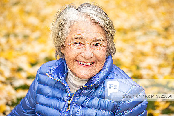 Porträt einer lächelnden hübschen älteren Frau vor gelben Blättern.