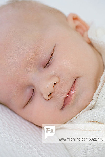 Lächelndes Gesicht eines 2 Monate alten Babys  das auf dem Rücken in seinem Bett schläft.