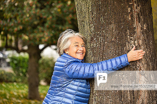 Porträt einer hübschen älteren Frau  die sich an einen Baum schmiegt.