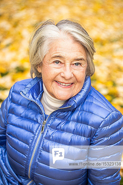 Porträt einer lächelnden hübschen älteren Frau vor gelben Blättern.