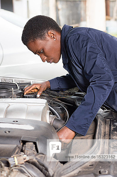 Junge Mechanikerin repariert ein Auto  indem sie den Motor in einen guten Zustand versetzt.