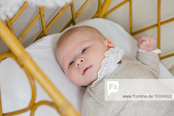 Porträt eines kleinen Babys in beigefarbener Kleidung von 2 Monaten  das in seinem Kinderbettchen liegt.