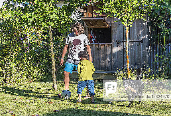 Zwei Jungen im Alter von fünf und dreizehn Jahren spielen mit einem Ball im Garten