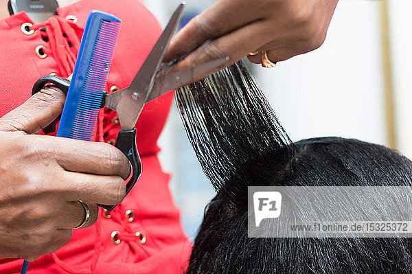 Die Friseurin ordnet die Haare ihrer Kundin  indem sie sie mit einer Schere schneidet.