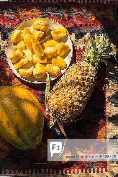 Jackfrucht-Segmente auf einem Teller  ganze Ananas und Papaya auf einem bunten Hintergrund