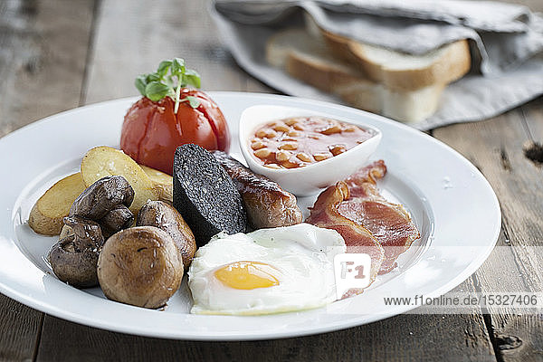 Englisches Frühstück  serviert auf einem weißen Teller mit Weißbrotscheiben im Hintergrund