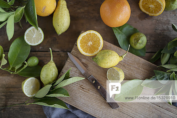 Bio-Orangen und -Zitronen mit einem Messer auf einem rustikalen Holzbrett