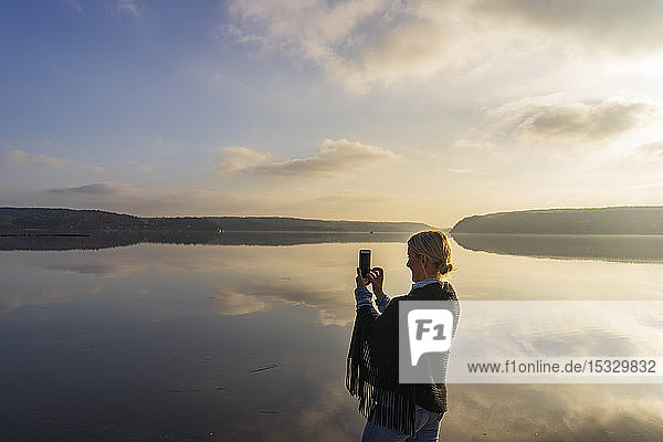 Mid adult woman holding cell phone in front of Lake Aspen in Lerum Sweden