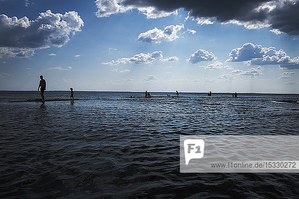 Silhouettes of people walking along sea under cloudy sky