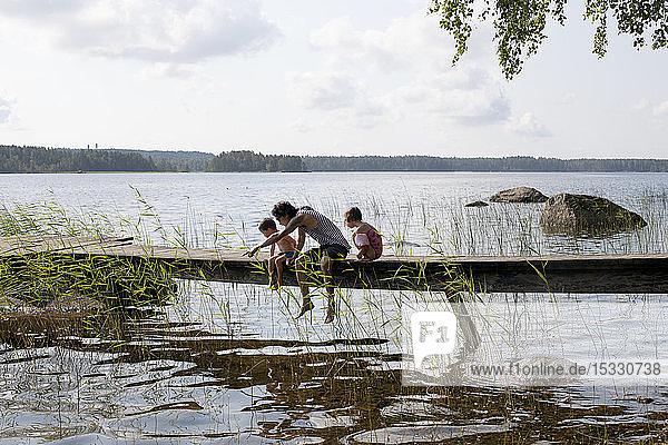 Mann sitzt mit seinen Kindern auf einer Seebrücke